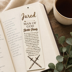 May include: A light-colored wooden bookmark featuring the name Jared, the text Man of God, Battle Ready, and a passage from Ephesians 6:10-12. The design includes a small hole at the top and a graphic of two crossed swords at the bottom.