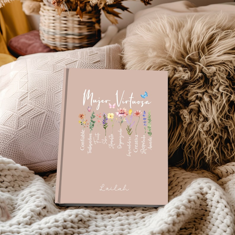 May include: A pink journal with the text "Mujer Virtuosa" in white lettering. The journal has a floral design with butterflies and the text "Confiable, Trabajadora, Fuerte,  Fiel,  De Amor,  Organizada,  Imparable,  Creativa,  Respetuosa,  Amigable" in white lettering. The journal is signed "Lailah" in white lettering.