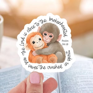 May include: A sticker featuring two cartoon monkeys hugging. One monkey is orange, the other is gray. The sticker has text that reads "The Lord is close to the brokenhearted and saves the crushed in spirit" with Psalm 34:18.