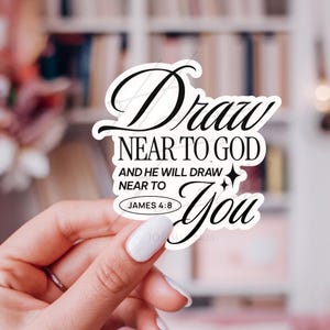 May include: A white sticker with black script that reads "Draw NEAR TO GOD AND HE WILL DRAW NEAR TO You" with "JAMES 4:8" in a small oval. The sticker is held by a hand with white nail polish.