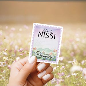 May include: A rectangular card with a purple border and the words "Jehovah Nissi" and "The Lord my Banner" in black script. The card features a watercolor design of mountains and flowers.