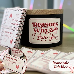 May include: A black candle with a wooden lid and a label that reads "Reasons Why I Love You" in red. Beside it are small cards with the same text and heart illustrations, designed to look like airmail envelopes. A romantic gift idea.
