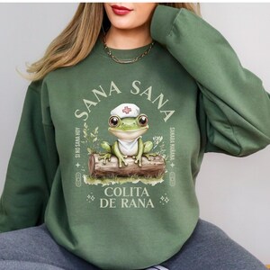 May include: Green sweatshirt with a frog wearing a nurse's hat and the text "Sana Sana Colita de Rana" in a circle. The text around the circle says "Si no sana hoy Sana Ma&ntilde;ana".