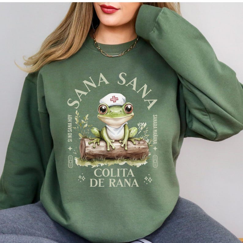 May include: Green sweatshirt with a frog wearing a nurse's hat and the text "Sana Sana Colita de Rana" in a circle. The text around the circle says "Si no sana hoy Sana Ma&ntilde;ana".