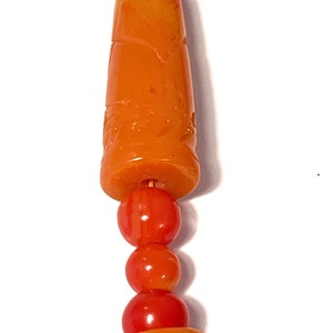 May include: A close-up of a necklace with orange and red beads. The beads are carved with intricate designs.