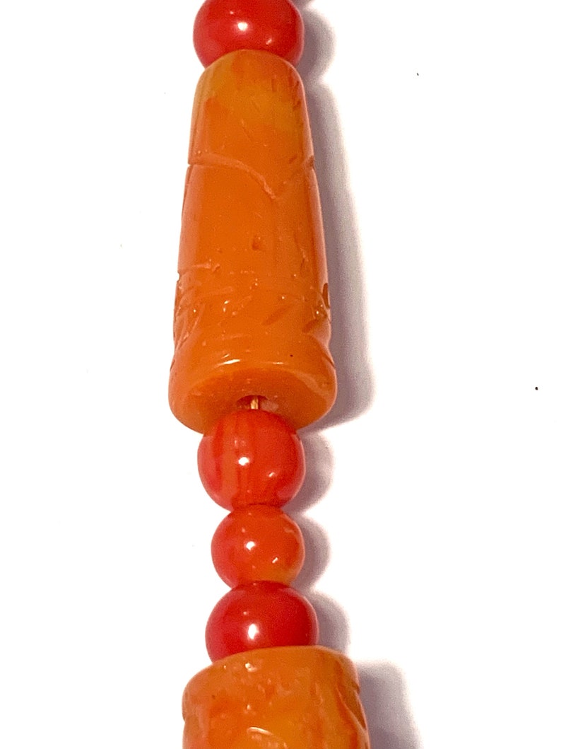 May include: A close-up of a necklace with orange and red beads. The beads are carved with intricate designs.