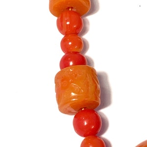 May include: A close-up of a necklace made of orange and red beads. The beads are round and have a smooth, polished finish. The necklace is strung on a thin wire.