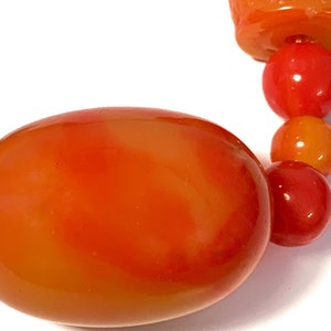 May include: A close-up of a large, orange, oval-shaped bead. The bead is made of glass or plastic and has a smooth, glossy finish.