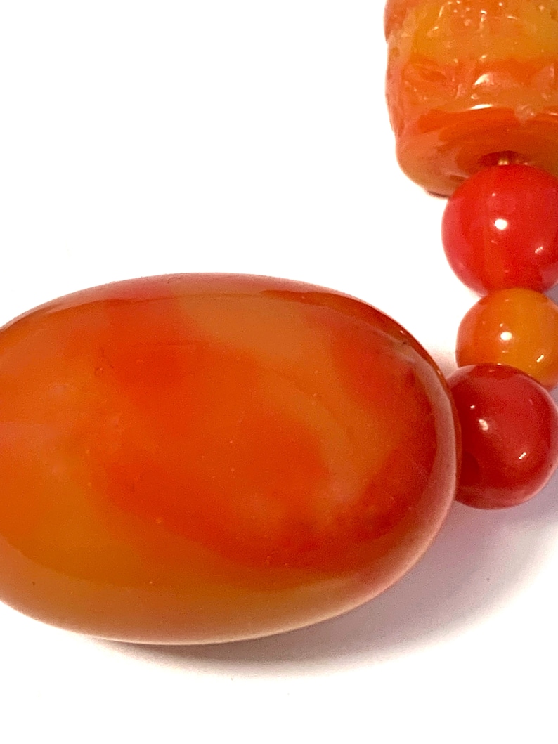 May include: A close-up of a large, orange, oval-shaped bead. The bead is made of glass or plastic and has a smooth, glossy finish.
