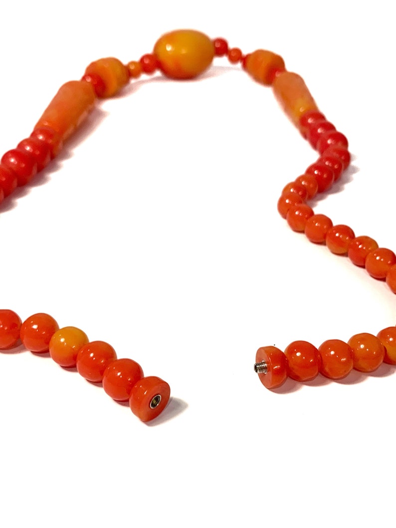 May include: A broken orange and yellow beaded necklace with a metal clasp. The necklace is made of round and oval beads.