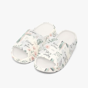 Puede incluir: Sandalias deslizantes blancas con un diseño floral y texto inspirador. Las sandalias presentan un patrón de flores rosas, hojas verdes y texto que dice "Covered in grace", "Rooted in Christ" y "She is worthy".
