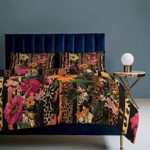 May include: A bed set featuring a vibrant floral and leopard print design. The bedding includes a duvet cover and pillowcases with large pink flowers, orange stripes, and animal print patterns. The set is displayed on a blue bed frame.