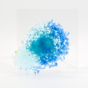 Puede incluir: Una pieza de arte abstracto azul y verde encerrada en un cubo de acrílico transparente. Los colores azul y verde se mezclan en un patrón de remolino.