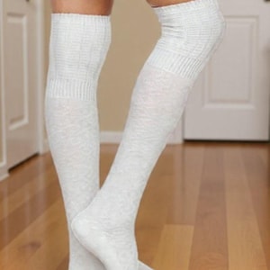 May include: A pair of white, textured, over-the-knee socks. The socks are made of a soft material and have a ribbed design at the top and around the knees. The socks are worn on a person's legs, with the feet visible.