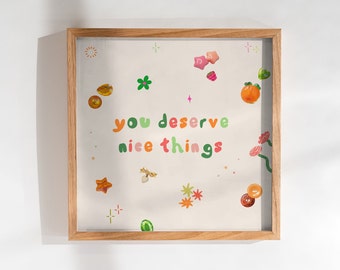 May include: A framed print with a white background and colorful illustrations of stars, flowers, and fruit. The text "you deserve nice things" is written in a colorful, playful font.