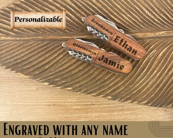 Puede incluir: Dos navajas de bolsillo de madera personalizadas con la palabra "Groomsmen" grabada en el mango, junto con los nombres "Ethan" y "Jamie".