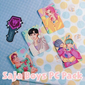May include: A collection of Saja Boys PC Pack items, including character art cards and a light stick. The cards feature colorful illustrations of male figures in various poses and outfits. The light stick has a purple lion emblem and the text "SajaBoys".