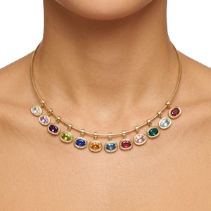 May include: A gold collar necklace featuring a series of twelve oval-cut gemstones in various colors, including purple, blue, green, yellow, pink, and red, suspended from a thin, curved gold bar that rests against the base of the neck.