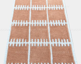 May include: A rectangular rug with a repeating pattern of peach-colored blocks separated by white lines. The blocks have a unique, textured design. The rug's edges are bordered with white. This rug is suitable for home decor.