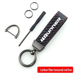 May include: Black leather keychain with a red stitching detail and a white "4RUNNER" logo. The keychain has a metal ring and a metal loop for attaching keys.