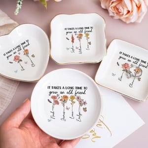 Könnte beinhalten: Eine Sammlung weißer Keramik-Schmuckschalen in Herz-, Quadrat- und runder Form. Jede Schale hat einen goldenen Rand, Blumenillustrationen, Schmetterlinge und den Text "IT TAKES A LONG TIME TO grow an old friend".