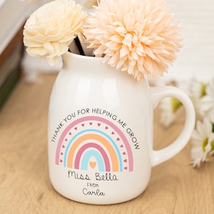 May include: White ceramic mug with a rainbow design and the text "Thank you for helping me grow. Miss Bella from Carla". The mug is filled with dried flowers.