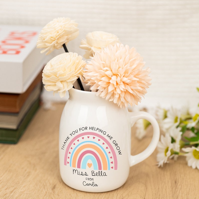 May include: White ceramic mug with a rainbow design and the text "Thank you for helping me grow. Miss Bella from Carla". The mug is filled with dried flowers.