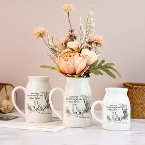 May include: Three white ceramic mugs and a vase with a floral arrangement. The mugs and vase have a handle and a Winnie the Pooh illustration with text that reads "Never forget the difference you make, Mrs. Glow. Thank you Brenda."