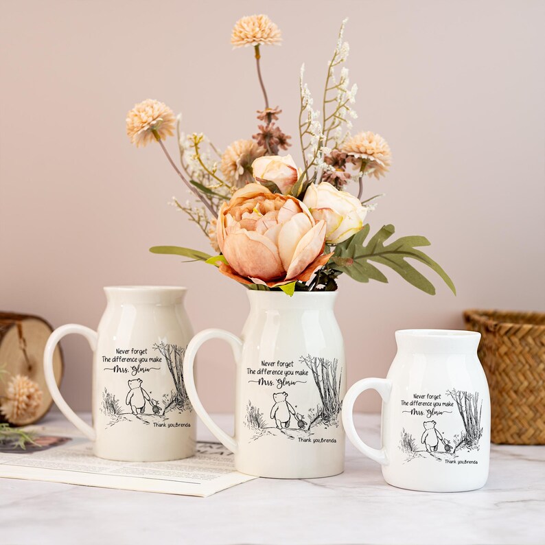 May include: Three white ceramic mugs and a vase with a floral arrangement. The mugs and vase have a handle and a Winnie the Pooh illustration with text that reads "Never forget the difference you make, Mrs. Glow. Thank you Brenda."