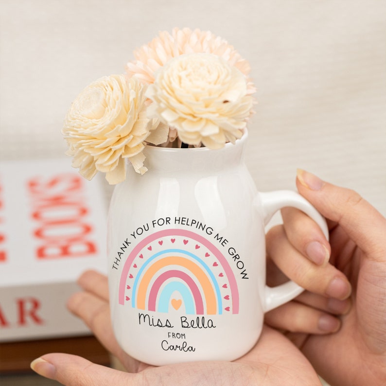 May include: White ceramic mug with a rainbow and heart design. The text reads "Thank you for helping me grow. Miss Bella from Carla".