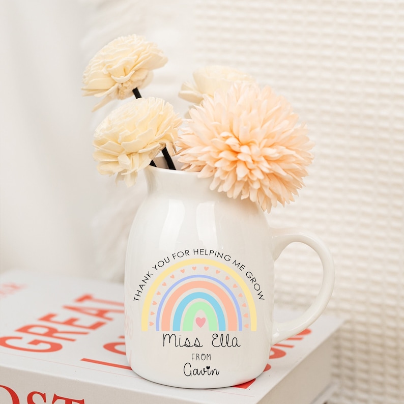 May include: White ceramic vase with a rainbow and the text "Thank you for helping me grow. Miss Ella from Gavin" on it. The vase is filled with dried flowers.