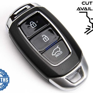 Op de afbeelding: Zwarte autosleutel met drie knoppen: vergrendelen, ontgrendelen en kofferbak openen. De sleutel heeft een zilveren rand en een blauw LED-lampje. De tekst "HOLD" staat op de knop voor het openen van de kofferbak. De afbeelding bevat ook een logo voor "MR KEY" en een garantie sticker met de tekst "6 MONTHS WARRANTY".