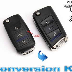 Op de afbeelding: Twee zwarte autosleutels met elk drie knoppen. De sleutelhanger links heeft een klein LED-lampje. De sleutelhanger rechts heeft een zilveren rand. De tekst "CUTTING AVAILABLE" is zichtbaar in de rechterbovenhoek van de afbeelding. De tekst "Conversion Kit" is zichtbaar in het midden onderaan de afbeelding.