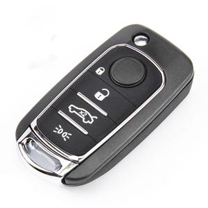 May include: A black rectangular car key fob with a metallic silver trim. The device features four rubberised buttons displaying icons for locking, unlocking, boot release, and light activation, along with a small circular hole for a keyring.
