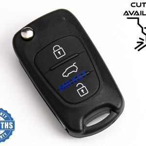 Peut inclure: Clé de voiture noire avec trois boutons. Les boutons ont des icônes pour déverrouiller, voiture et verrouiller. Le porte-clés a un bouton argenté sur le dessus. Le texte "MR KEY" est imprimé sur le porte-clés en bleu. Le texte "CUTTING AVAILABLE" est imprimé en noir au-dessus d'un graphique d'un outil de coupe. Un autocollant circulaire bleu et blanc avec le texte "6 MONTHS WARRANTY" est dans le coin inférieur gauche de l'image.