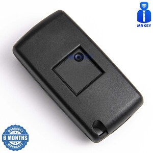 May include: Black plastic car key fob with a single button. The key fob has a small square button with a round hole in the center. The key fob is on a white background.