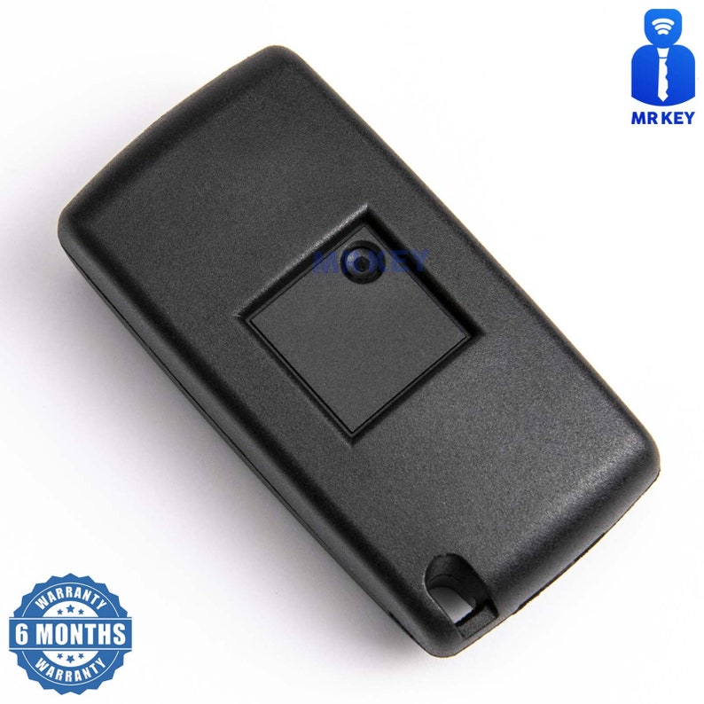 May include: Black plastic car key fob with a single button. The key fob has a small square button with a round hole in the center. The key fob is on a white background.