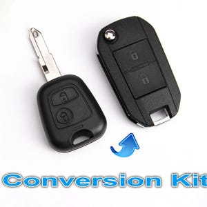 May include: A black car key fob conversion kit featuring a metal key blade attached to a plastic remote housing with two lock and unlock buttons, alongside a separate black plastic flip-style key fob casing with a silver button and text Conversion Kit.