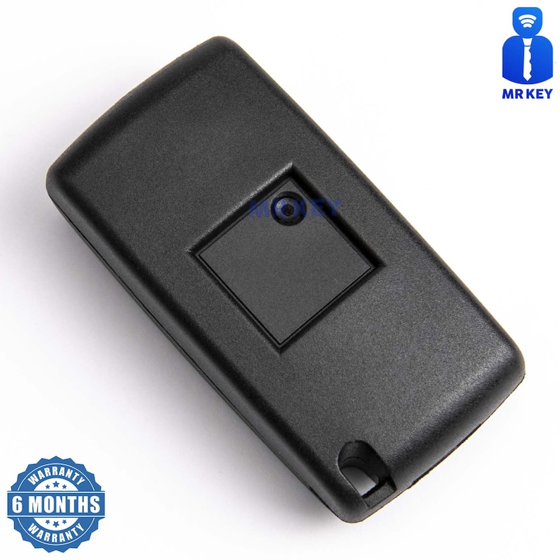 May include: Black plastic car key fob with a single button. The key fob has a small square button with a round hole in the center. The key fob is on a white background.