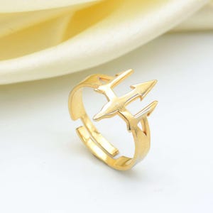 Puede incluir: Un anillo de color dorado con un diseño de doble flecha. El anillo es ajustable y tiene un estilo simple y moderno.