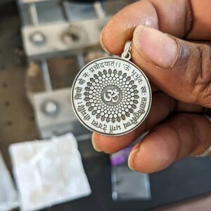 May include: Silver pendant featuring an Om symbol and Sanskrit text. The text reads "ऊ भूर्भुव स्व: तत्सवितुर्वरेण्यं भर्गो धीमहि। थियो यो नः प्रचोदयात् ।। 'ऊ भूर्भुव"