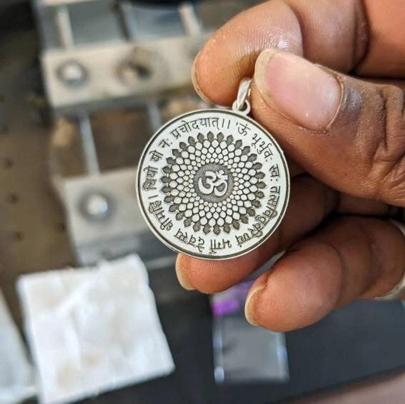 May include: Silver pendant featuring an Om symbol and Sanskrit text. The text reads "ऊ भूर्भुव स्व: तत्सवितुर्वरेण्यं भर्गो धीमहि। थियो यो नः प्रचोदयात् ।। 'ऊ भूर्भुव"
