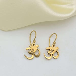 May include: A pair of gold-toned earrings featuring the Om symbol. The earrings are dangle style with a simple hook closure.
