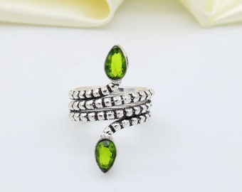 Può includere: Un anello a forma di serpente in argento con due pietre preziose verdi a forma di pera. L'anello è avvolto e ha una superficie testurizzata.