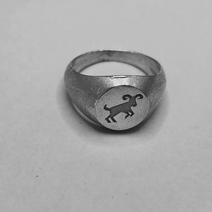 Może przedstawiać: Srebrny pierścień sygnetowy z grawerowanym wzorem stylizowanego barana.
