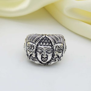 May include: Silver ring with three faces of Buddha, each with intricate details. The ring is a statement piece with a unique design.