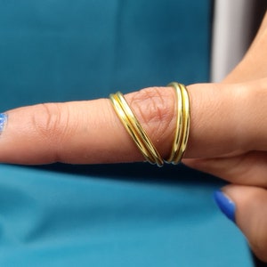 May include: A close-up of a finger wearing three gold rings. The rings are stacked on top of each other and are all the same width. The finger is painted with blue nail polish.