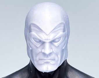 May include: A close-up of a white plastic action figure head with a black mask. The figure has a serious expression and is wearing a black suit.