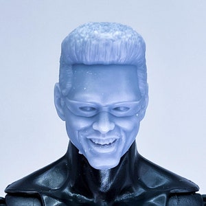 May include: A close-up of a gray plastic action figure head with a short, slicked-back hairstyle. The figure has a neutral expression with a slight smile and is wearing sunglasses.