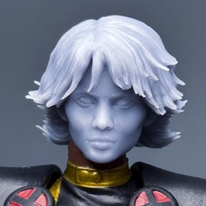 May include: A detailed action figure of Storm from the X-Men. The figure has a light blue complexion, white hair, and a black costume with gold accents and red and black circular shoulder emblems.